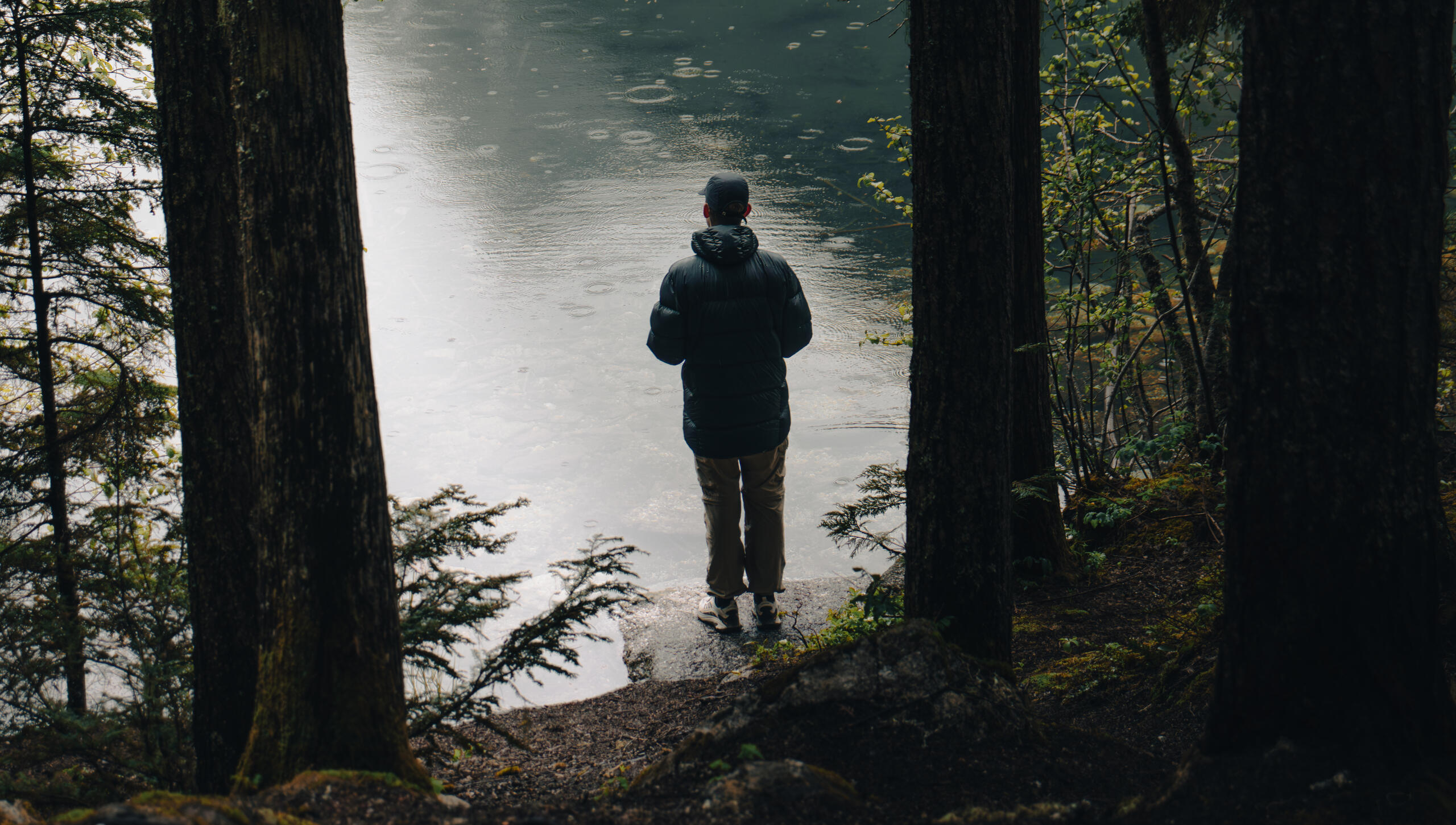 Throw Your Ideas Out There A portrait and landscape photo of a man in colorful clothing walking on rocky terrain throwing a large log upwards with the ocean, Victoria British Columbia and blue sky in the background.