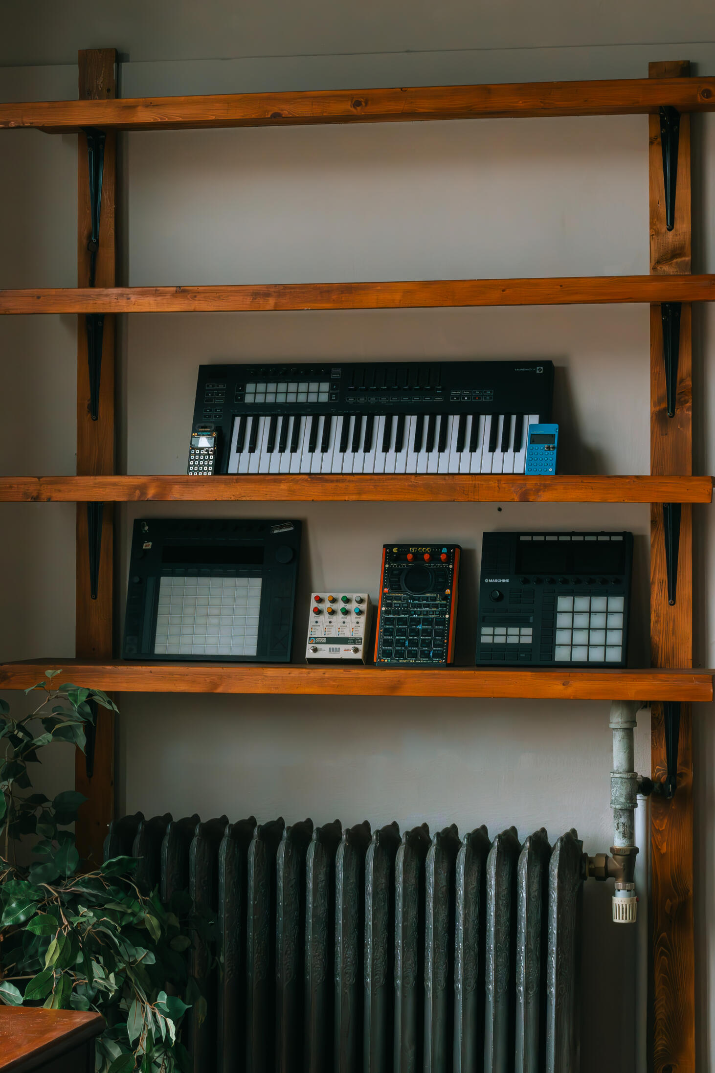 Vault 22 Multiple high-quality MIDI pianos and devices used to produce, mix, and master different music tracks, featured on a clean wood shelf with light shining on them.