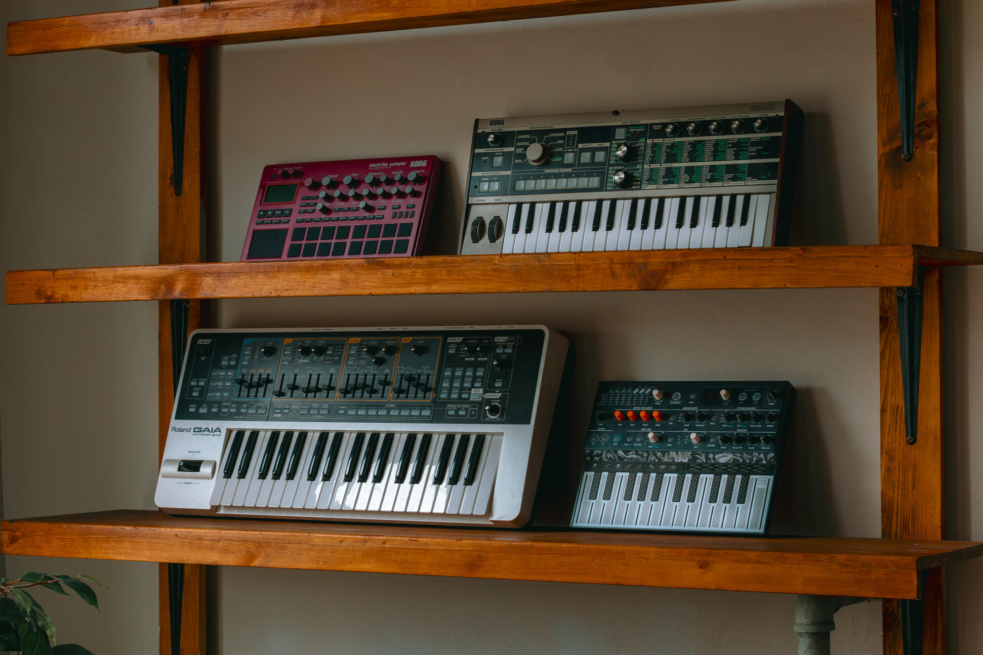 Vault 22 Four high-quality MIDI pianos and devices used to produce, mix, and master different music tracks, featured on a clean wood shelf with light shining on them.