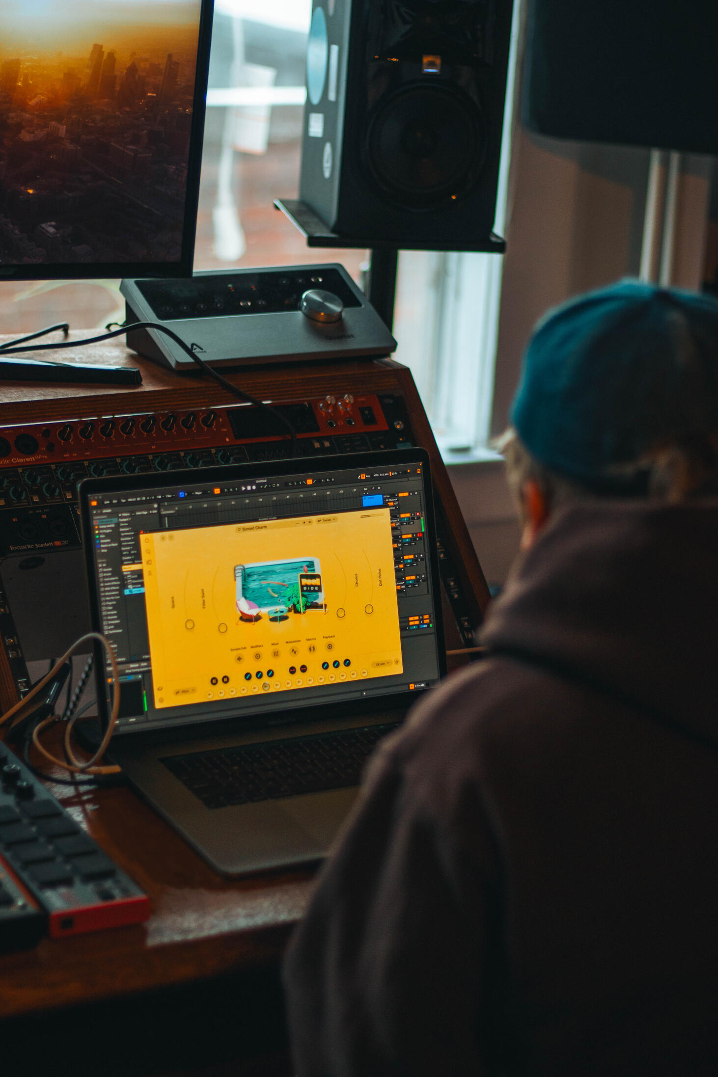 Vault 22 A man in a denim blue baseball cap sitting in front of a laptop and mixing desk with an Ableton plugin designed for making new sounds for music on the screen.