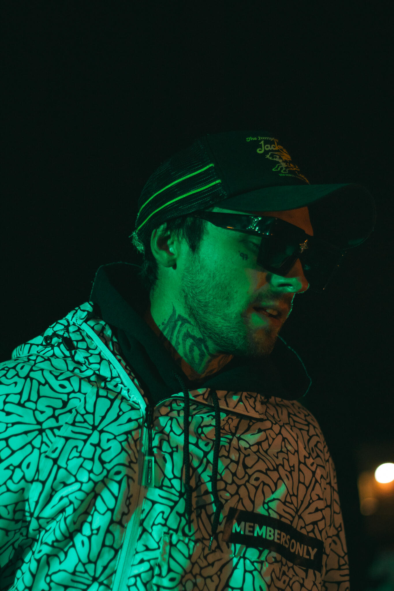 Never Ending Summer A man wearing a hat and Members Only jacket stands on stage in a dimly lit environment, creating a mysterious atmosphere while he performs rap music.