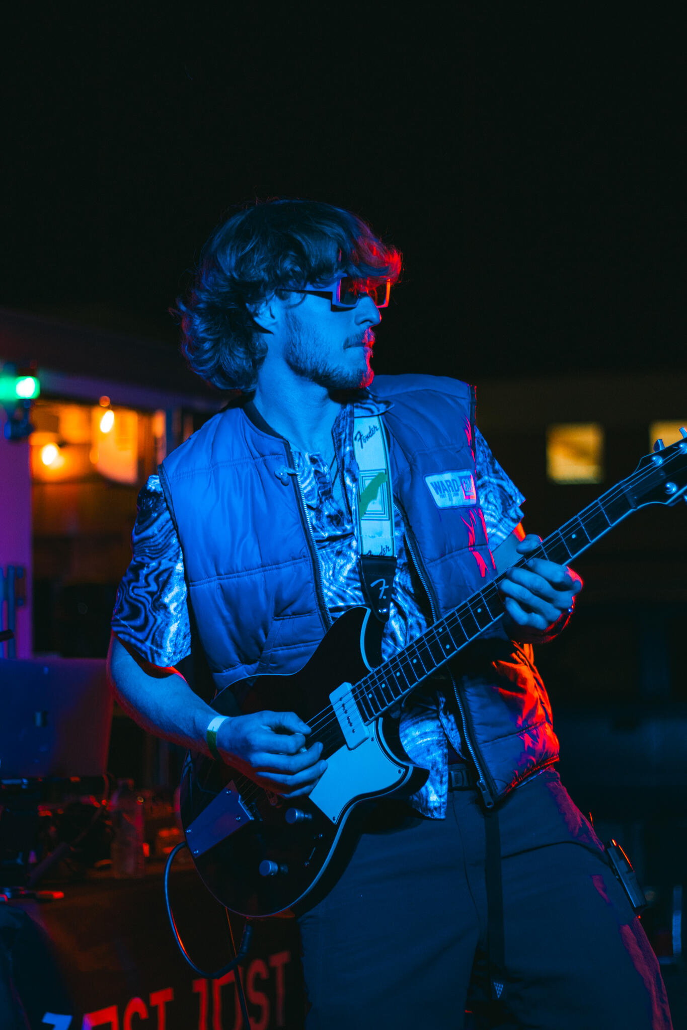 Never Ending Summer A man playing an electric guitar at Vice and Virtue brewery, immersed in his performance, with a warm neon ambiance surrounding him.