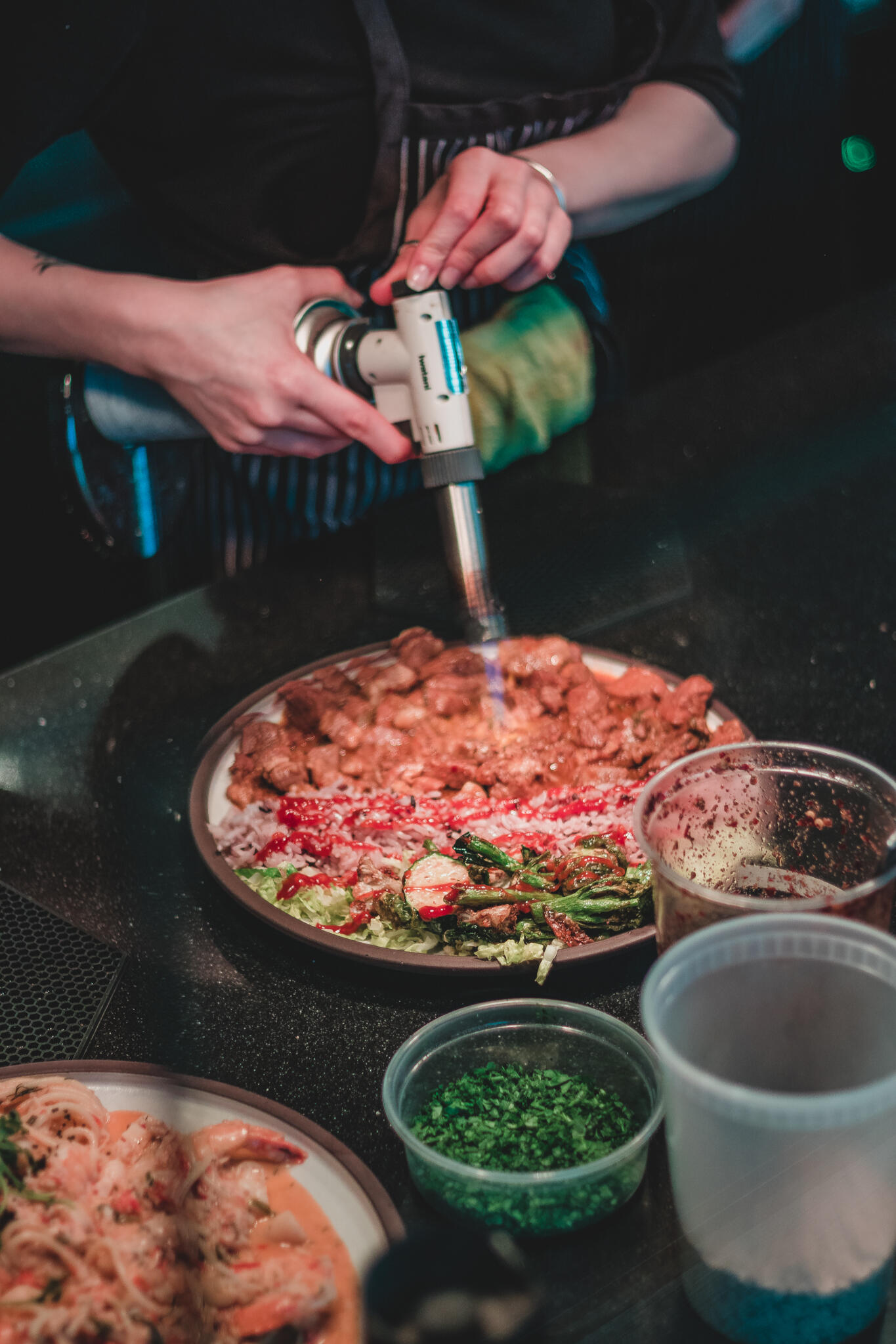 Gather Restaurant A chef using a food torch to finish of his Korean Italian infusion dish on a nice countertop with other ingredients surrounding it.